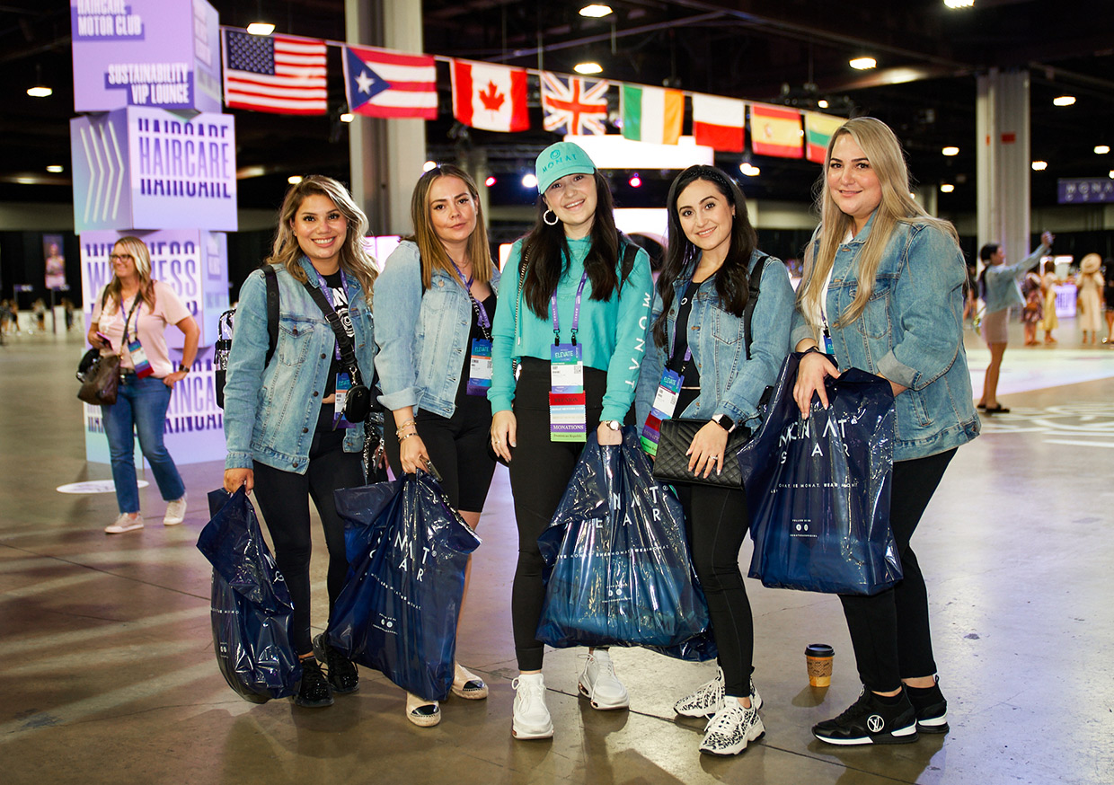 A group of Market Partners at the MONAT expo standing near a display of flags where MONAT is avaliable around the world. 