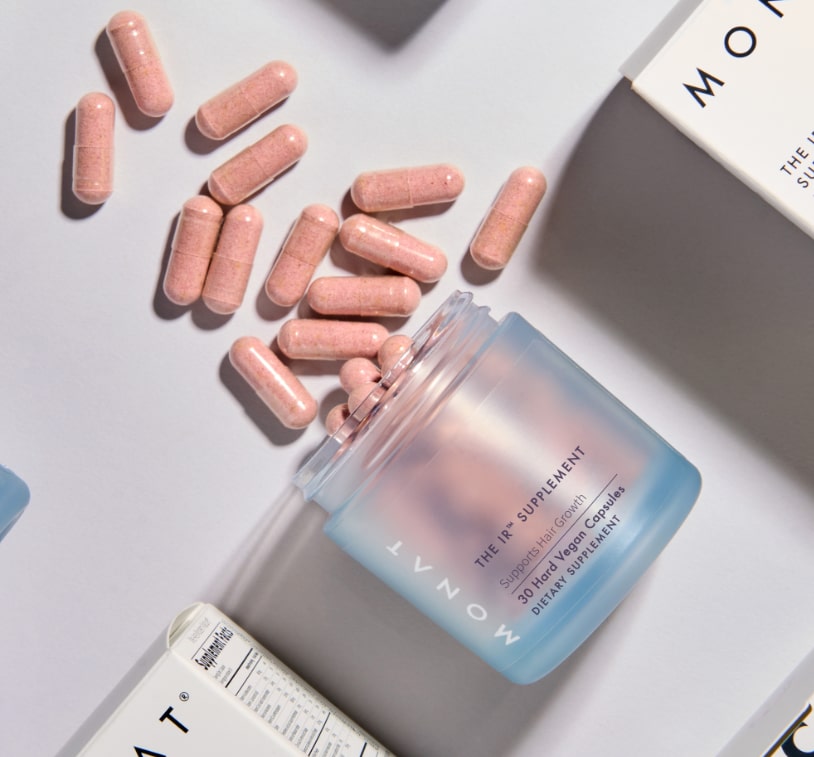An overhead view of the MONAT supplement bottle nestled among white product boxes with black text
