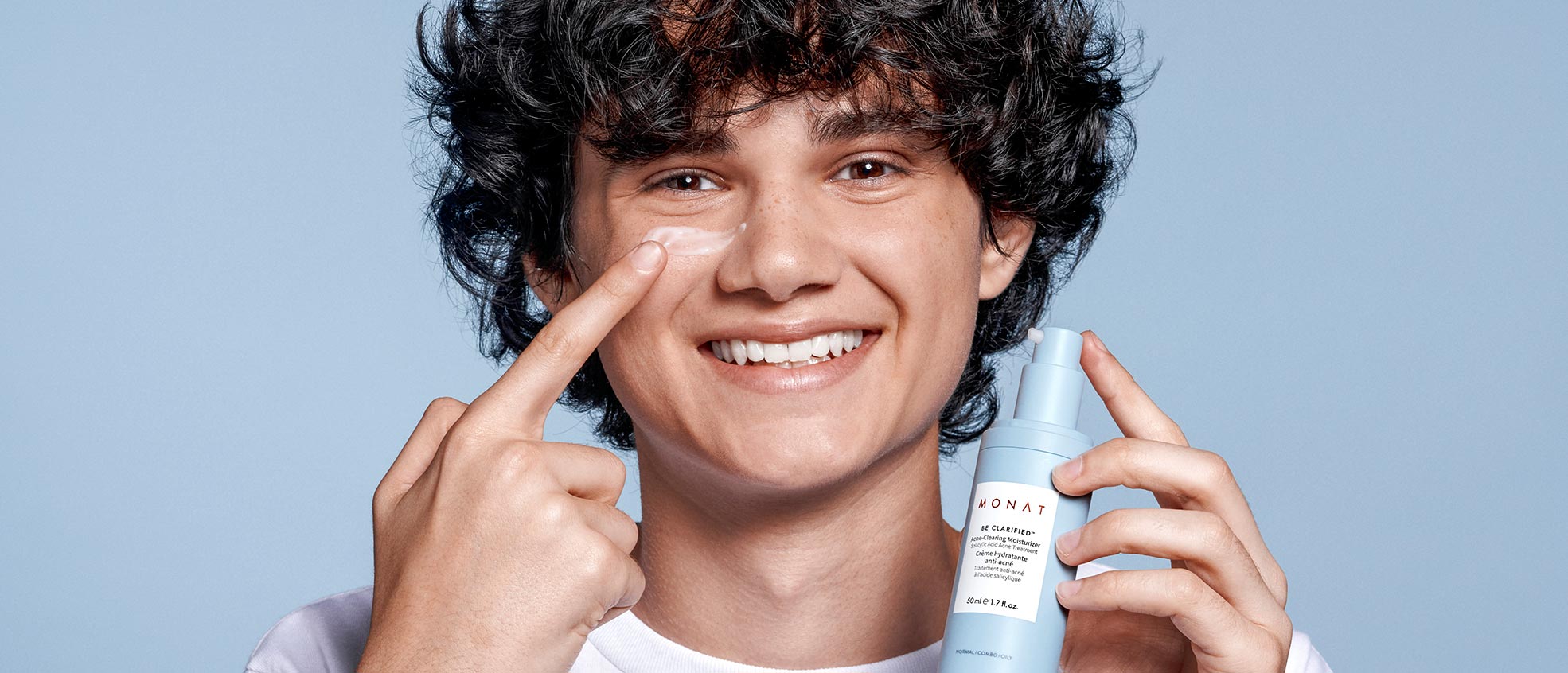 A  male smiling while applying BE CLARIFIED™ Acne-Clearing Moisturizer to his face. 