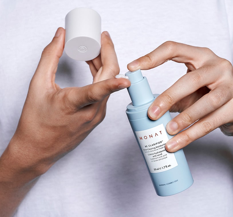 Hands holding BE CLARIFIED™ Acne-Clearing Moisturizer, while pumping the product onto fingertips. 