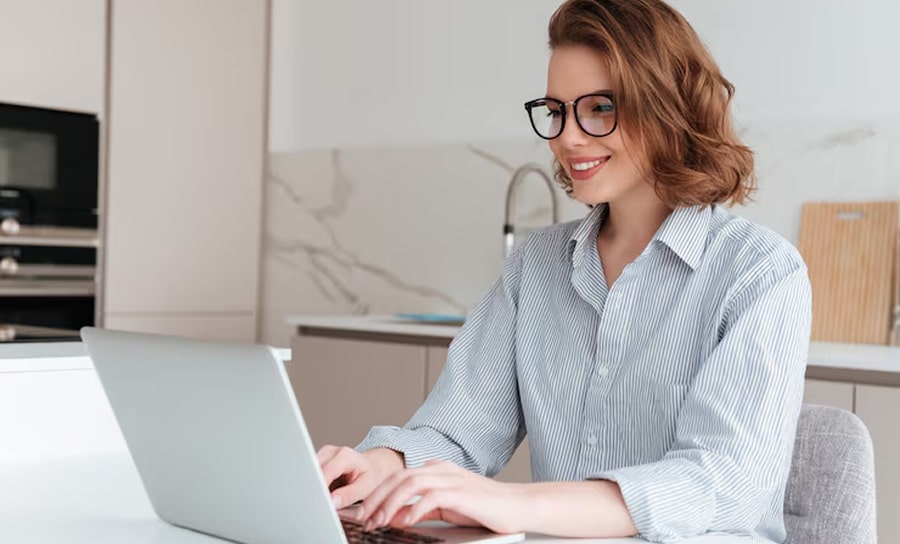 Woman using a laptop at home, smiling while working online.
