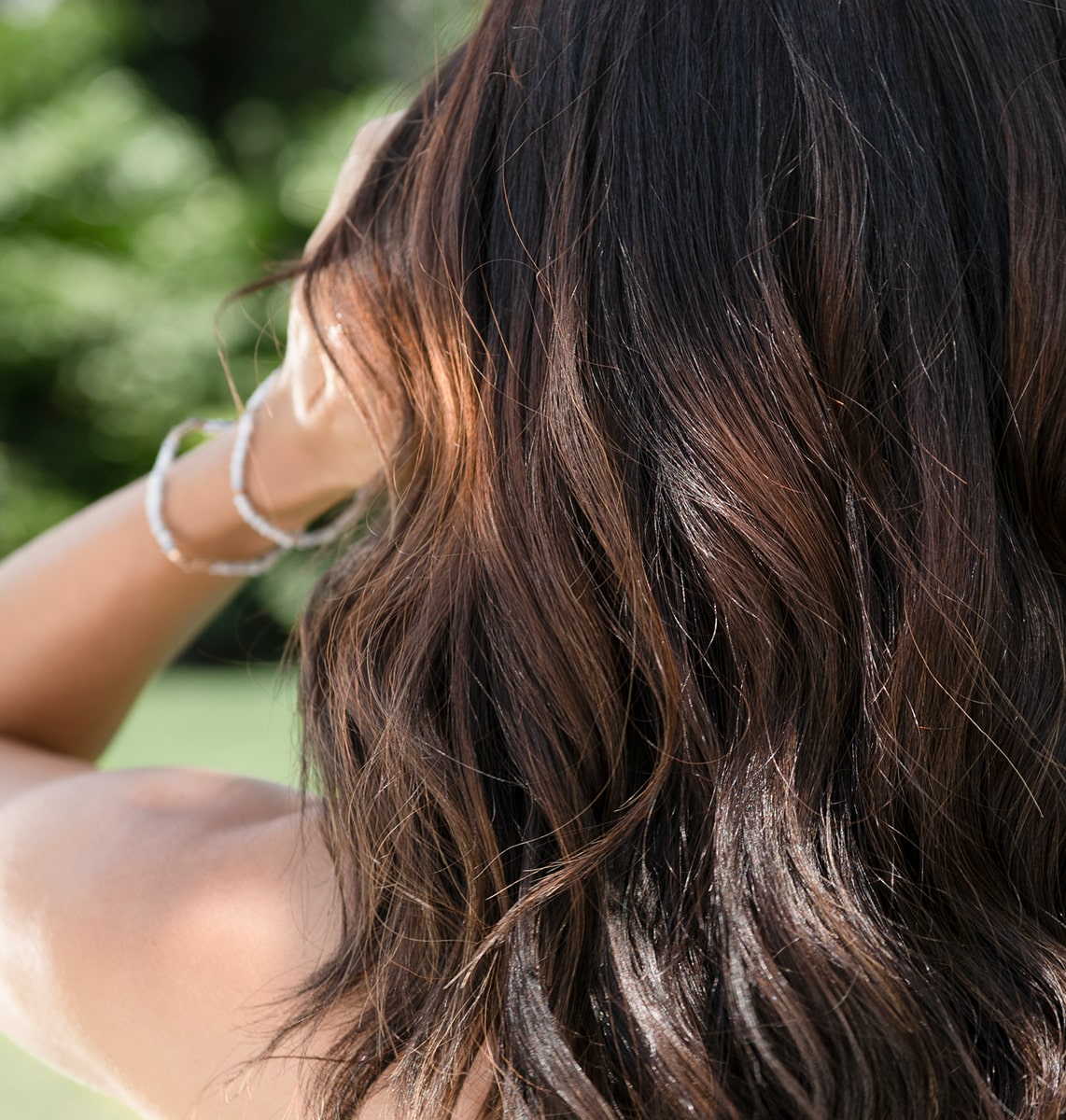 A close-up of a woman running her hand through her shiny, healthy hair.