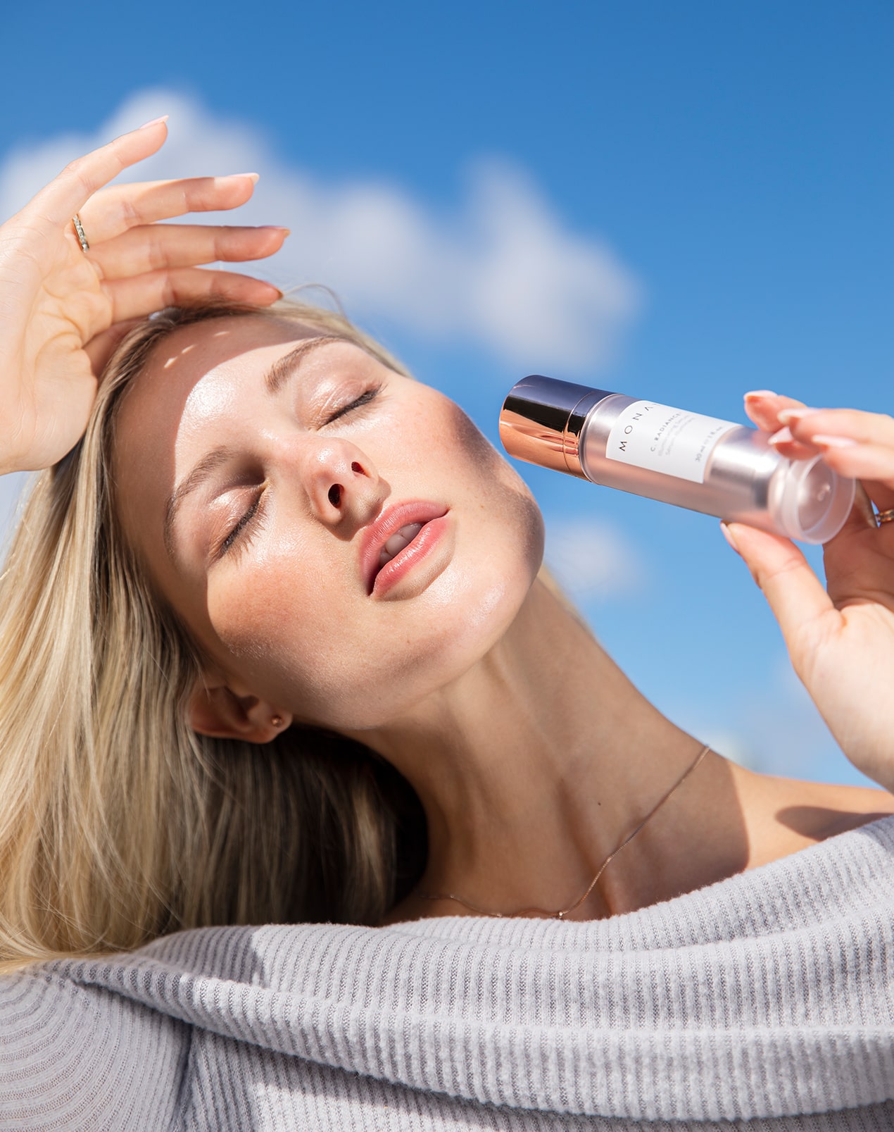 A woman lying down holding a skincare product with a relaxed expression.
