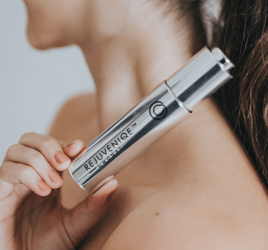 An african-american woman looking directly at the camera while applying the serum with the eyedropper. Left hand showcases MONAT's Hydration Booster.