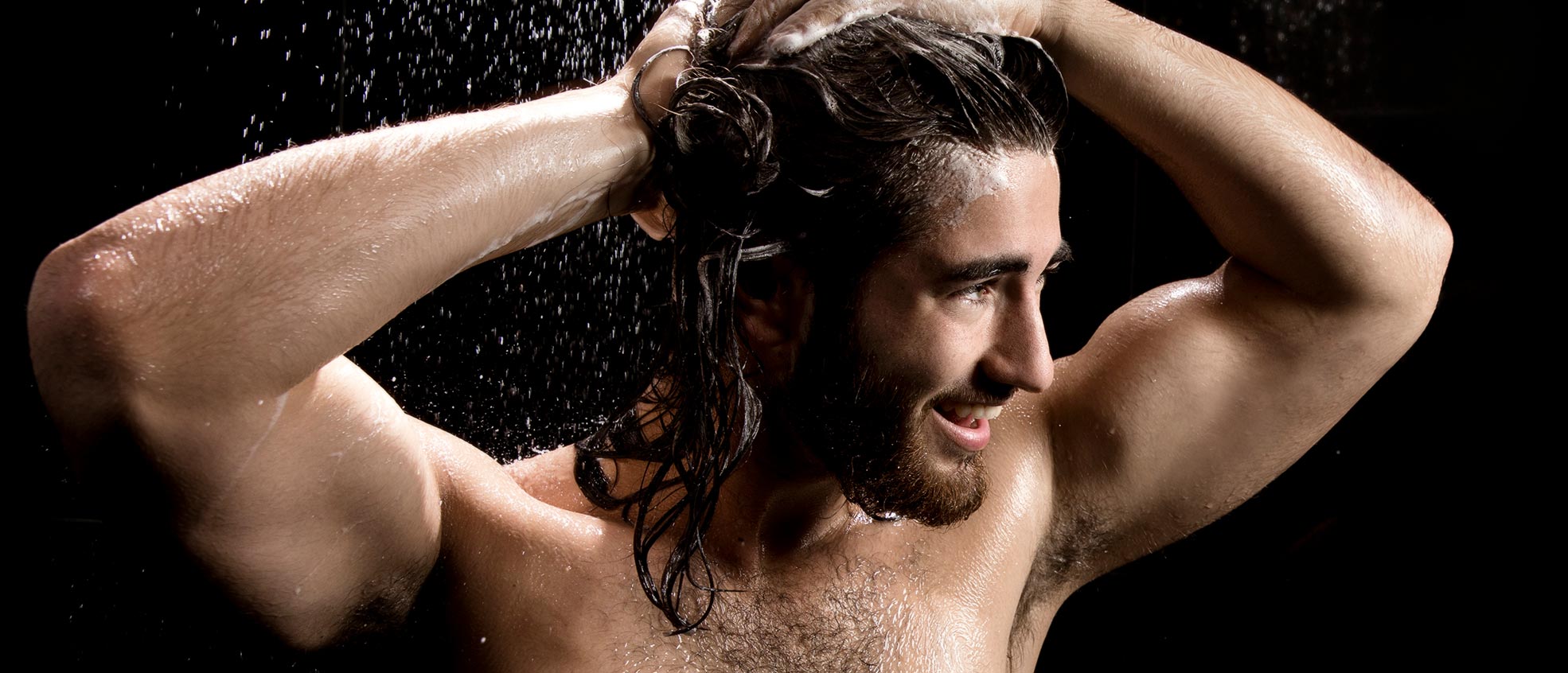 Male with long, brown hair washing his hair with MONAT Black Shampoo + Conditioner