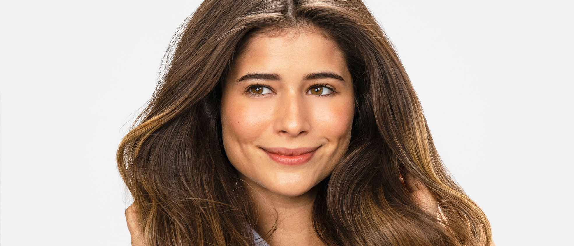 Mujer castaña sonriendo mientras sujeta su voluminoso cabello.