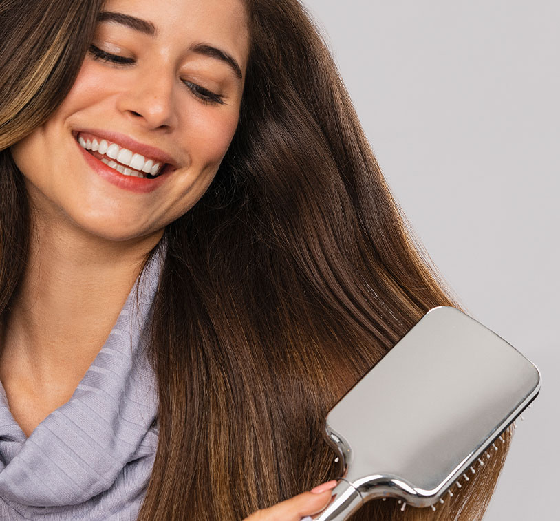 Mujer castaña sonriendo y cepillándose el cabello sobre un brillante fondo púrpura.