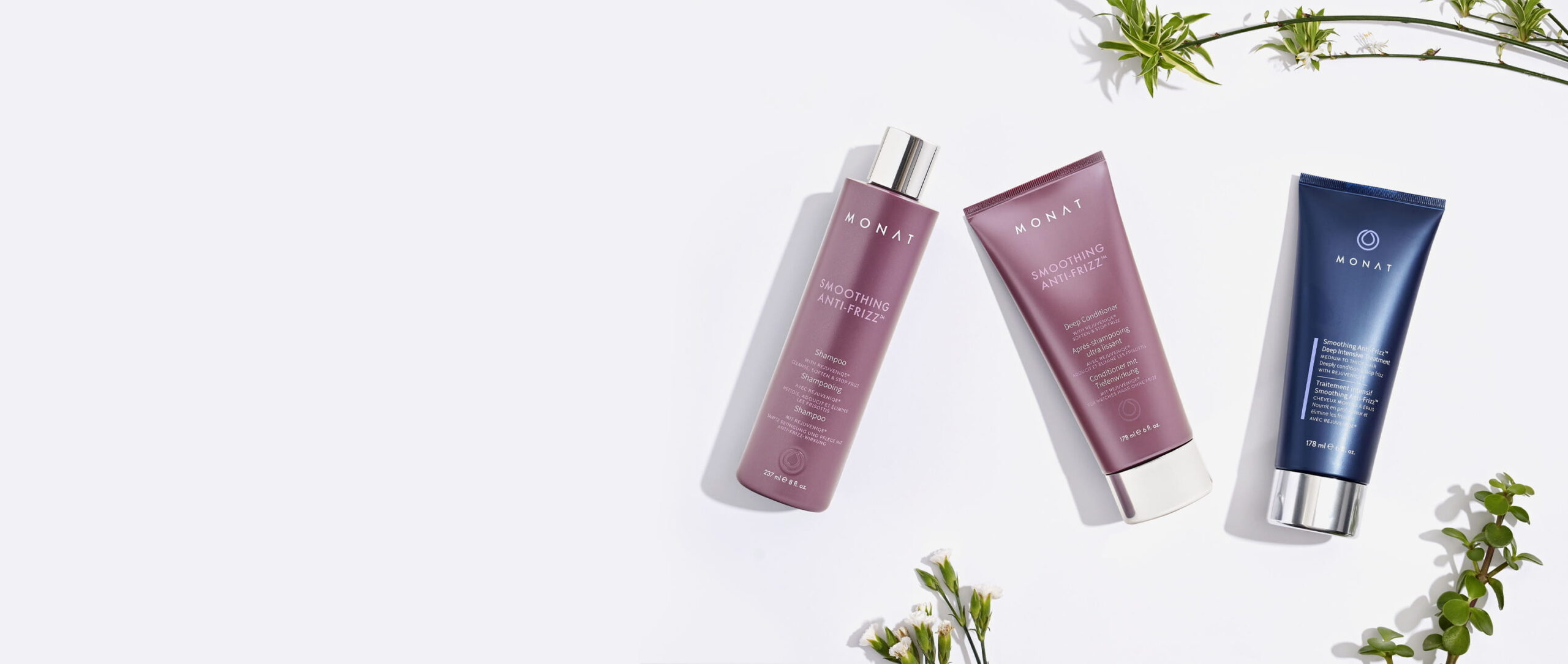 MONAT Smoothing Anti-Frizz shampoo, conditioner, and treatment on a white surface with greenery.