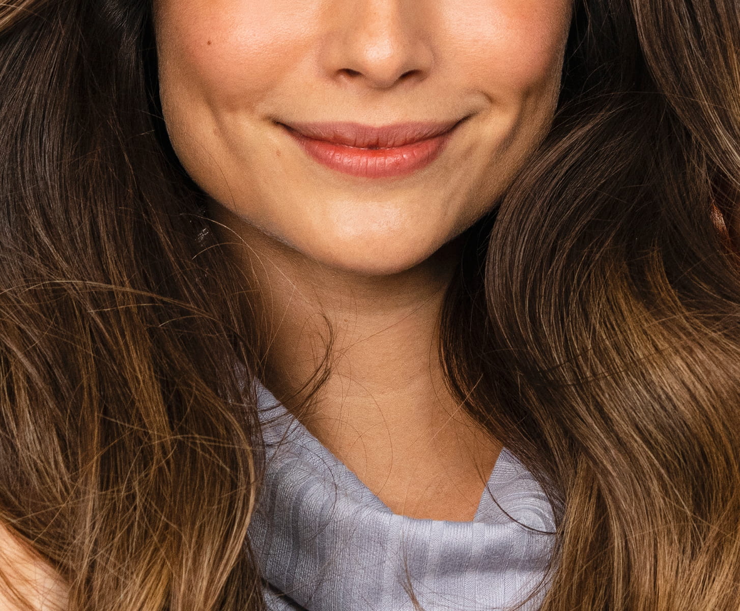 A woman with long, glossy brown hair smiles while holding a white bottle of MONAT Bond IQ Fortifying Shampoo.