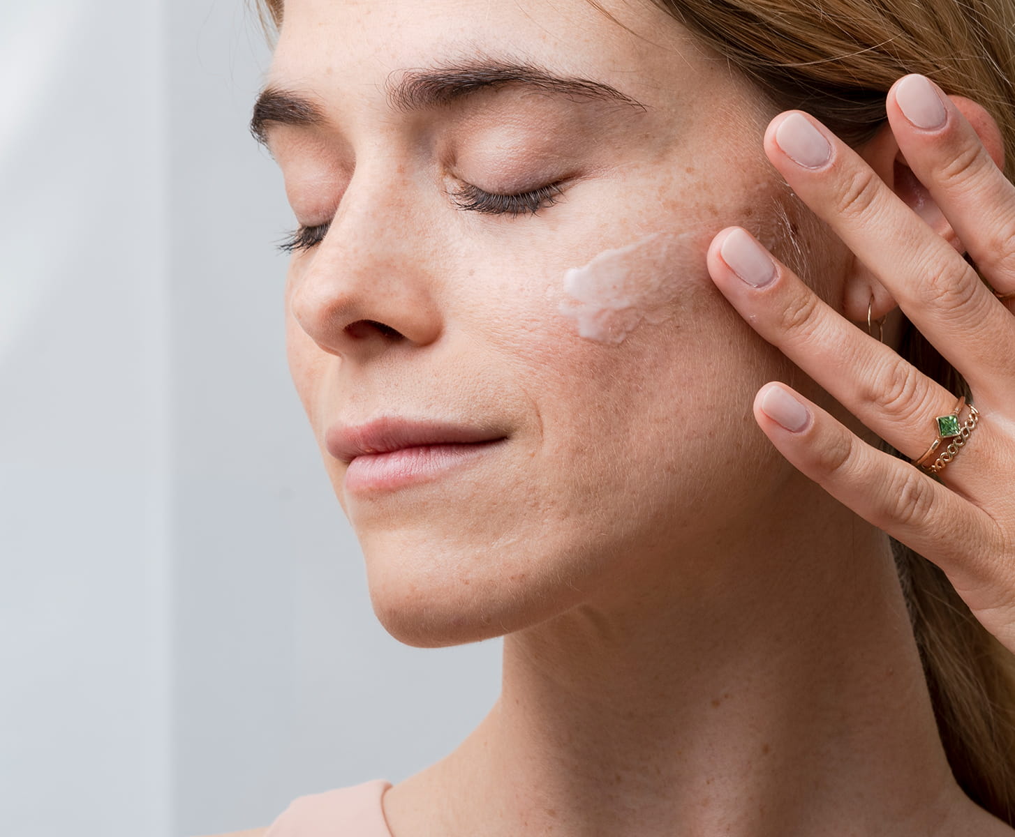 Smiling woman holding MONAT Barrier Booster™ Barrier Defense Moisturizer jar near her cheek.
