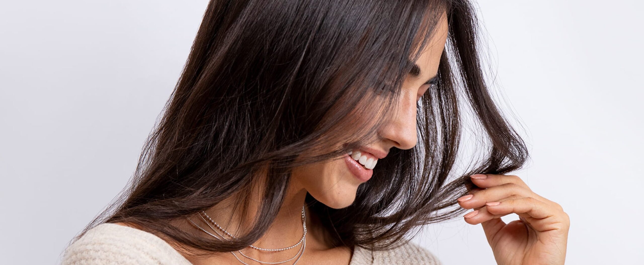 A woman with long, glossy brown hair smiles while holding a white bottle of MONAT Bond IQ Fortifying Shampoo.