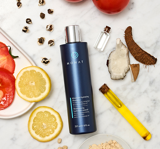 Advanced Hydrating Shampoo laying on a flat surface, along with ingredients such as lemon slices, coconut pieces, tomatoes and oil.