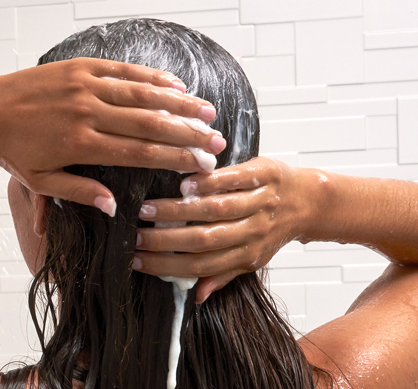 Brunette female washing her hair in the shower with Advanced Hydrating Shampoo, overlaying a texture shot of Advanced Hydrating Shampoo.