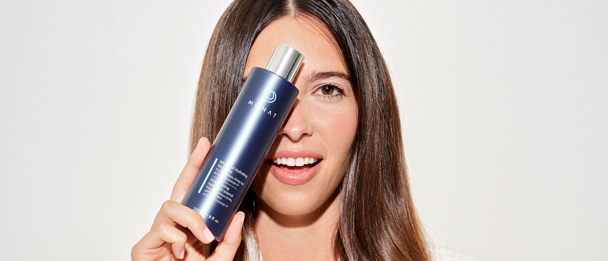 Brunette female holding the Advanced Hydrating Shampoo in front of her face.