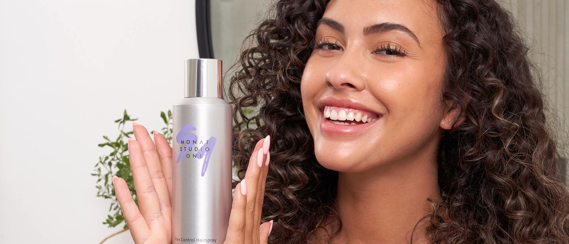 	Brunette female smiling while holding MONAT STUDIO ONE™ Flex Control Hairspray.