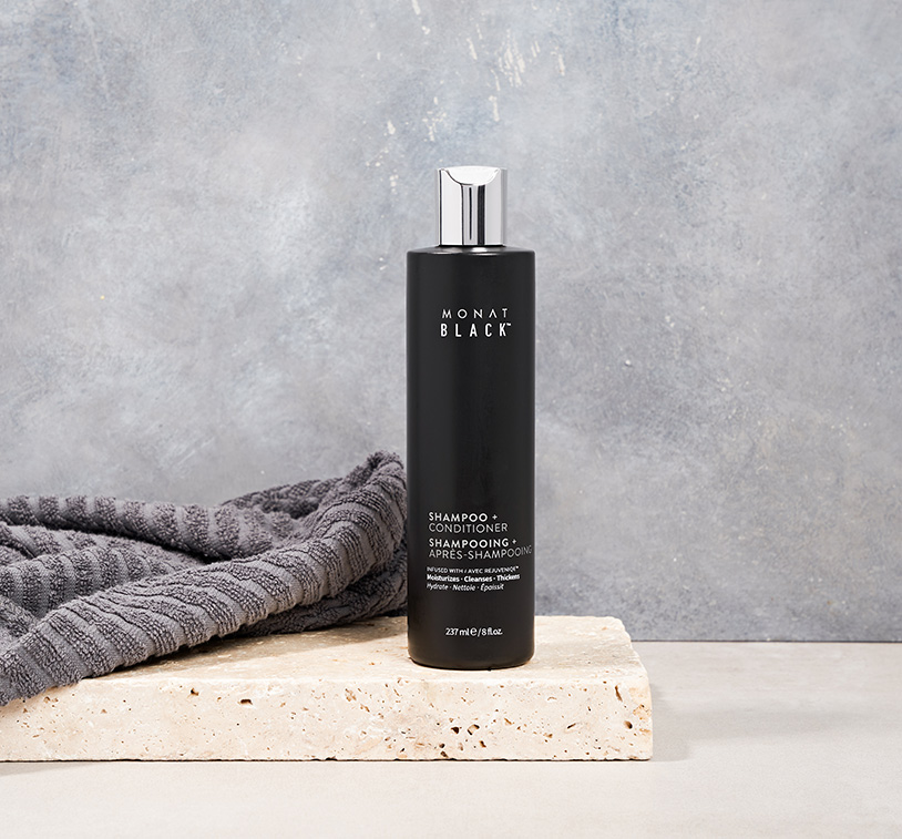 MONAT Black Shampoo + Conditioner standing on a piece of stone