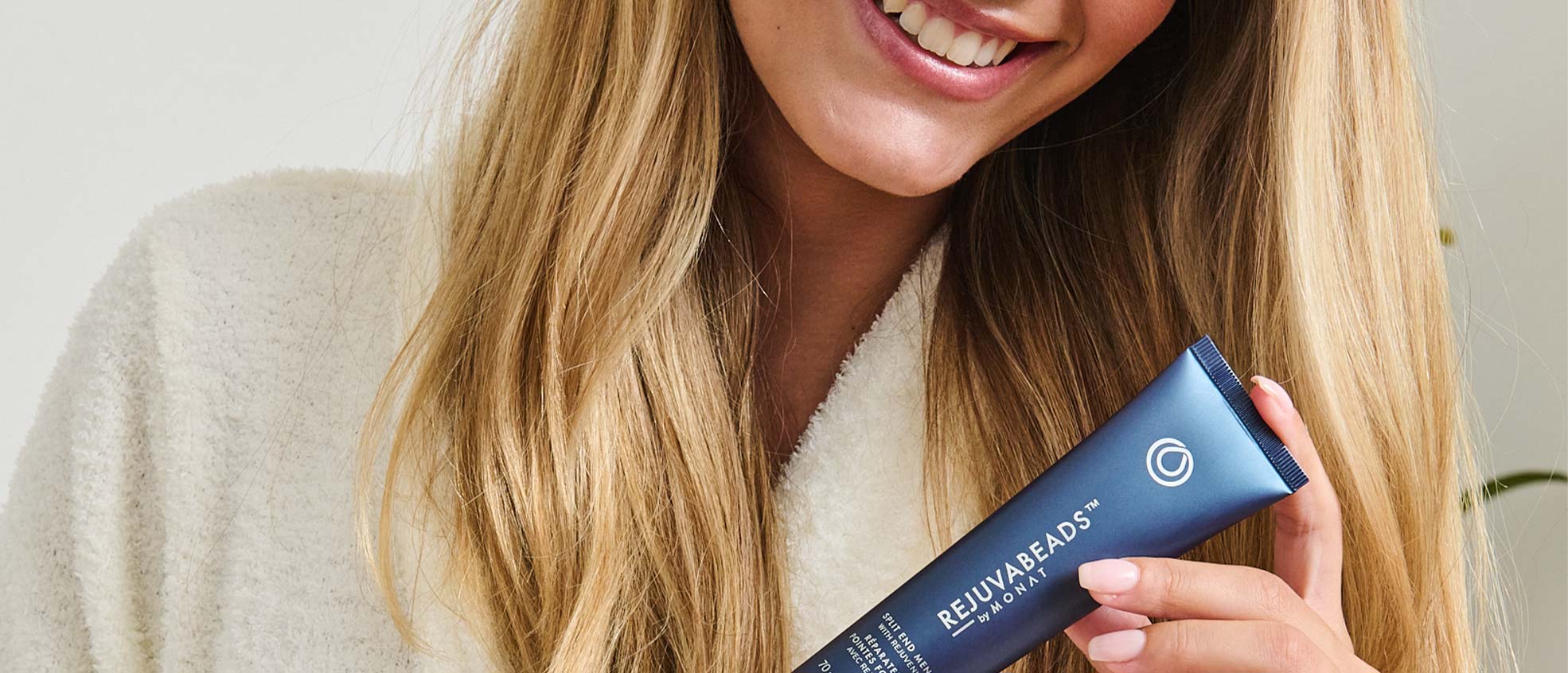 A blonde female smiling while holding REJUVABEADS® by MONAT