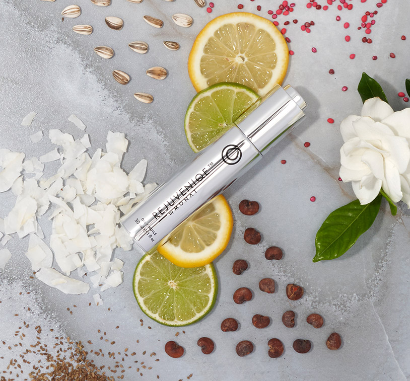 REJUVENIQE® laying on a flat surface, along with ingredients such as lemon and lime slices, sunflower seeds, coconut shavings and a white flower