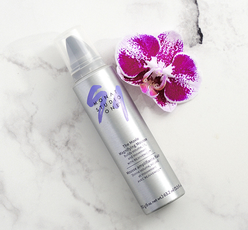 MONAT STUDIO ONE™ The Moxie Magnifying Mousse on a marble surface, next to a purple orchid.