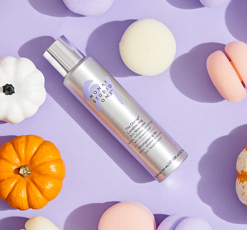 MONAT STUDIO ONE™ The Champ Conditioning Dry Shampoo laying on a purple surface with hair rollers and small pumpkins.