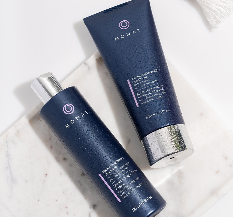 Volumizing Revive Shampoo and Volumizing Revitalize Conditioner laying on a flat marble surface.