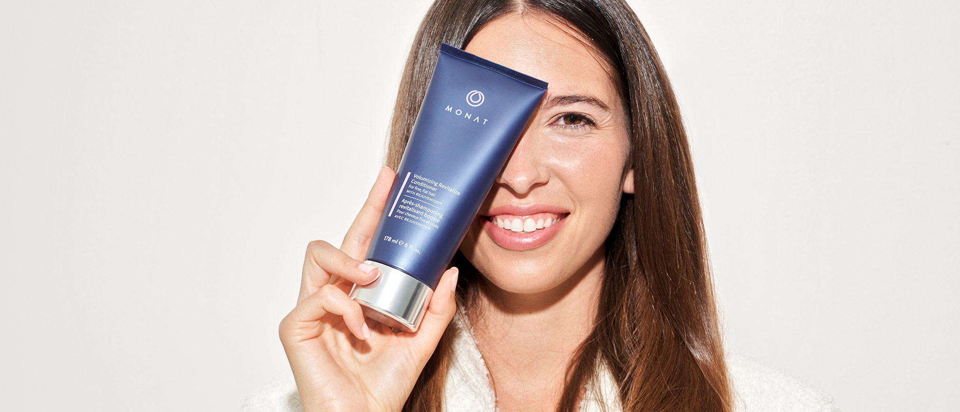 Brunette female holding the Volumizing Revitalize Conditioner in front of her face.
