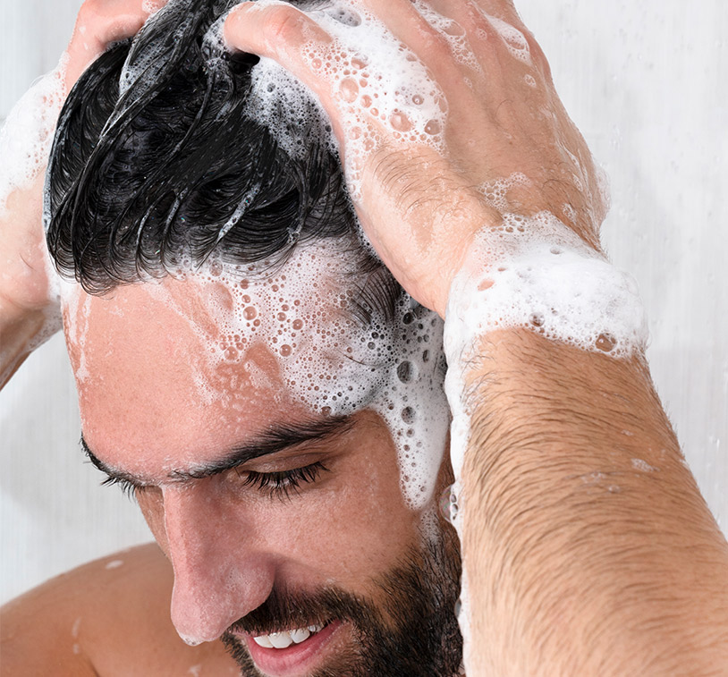 Male washing his hair with MONAT Black Shampoo + Conditioner, overlaying a photo of water