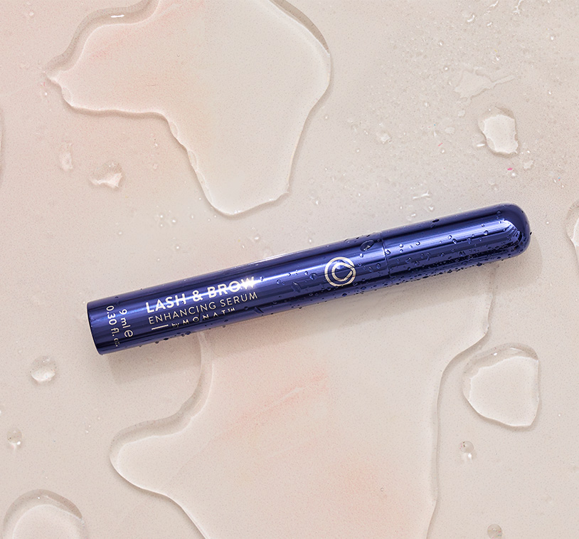 Lash & Brow Enhancing Serum laying on a flat surface with water droplets