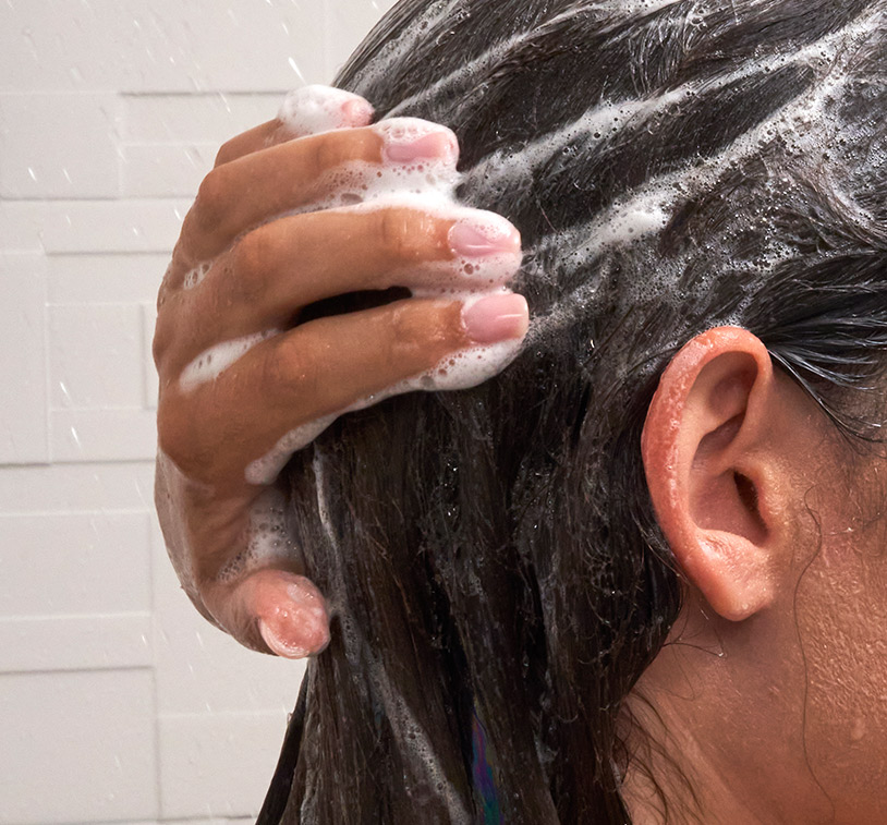 Brunette female washing her hair in the shower with Volumizing Revive Shampoo.