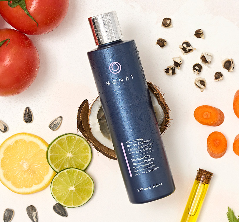 Volumizing Revive Shampoo laying on a flat surface, along with ingredients such as emon slices, coconut pieces, tomatoes, carrots and oil.