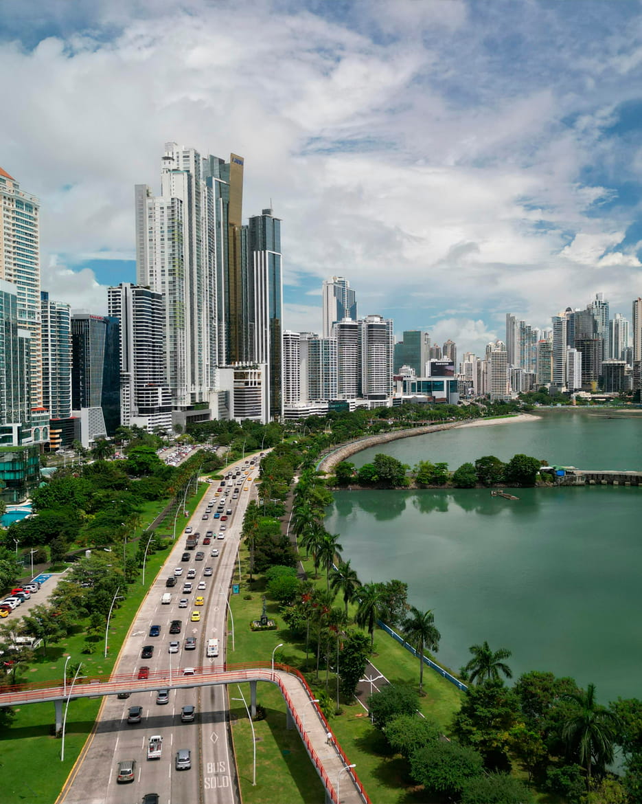 Modern skyline of Panama City, Panama, with high-rise buildings along a coastal road and green waterfront.