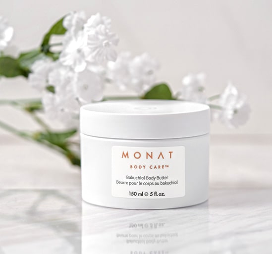 A product shot of MONAT BODY CARE™ Bakuchiol Body Butter on top of a marble stone in front of bunch of white flowers.