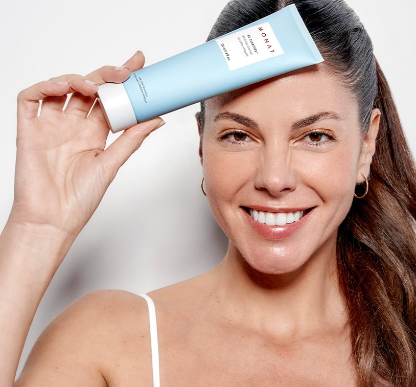 A brunette female holding BE CLARIFIED™ Acne Gel-Cream Cleanser infront of her forehead, while overlaying a texture shot of the cleanser. 
