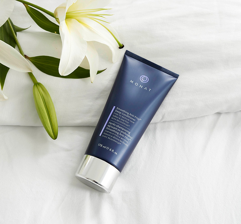 Smoothing Anti-Frizz™ Deep Conditioner laying on a white sheet, next to white flowers.