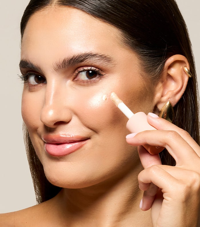 A brunette woman applying MONAT Makeup on one of her cheekbones.