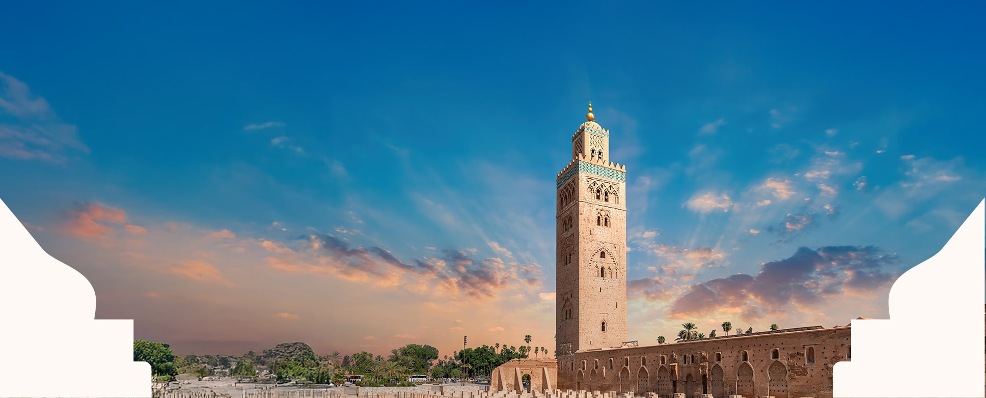 A Moroccan-style tower stands prominently in the heart of the city, showcasing its elegance. It rises majestically against a blue sky, with the sunset light enhancing its magnificence.