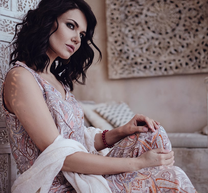 A woman wearing a vibrant, colorful dress is seated gracefully on a chair, exuding elegance and style.