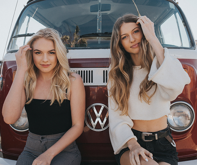 Two young women sitting behind their funky 70’s van showing off their revived hair once they found our what is clarifying shampoo and what it could do for their hair.