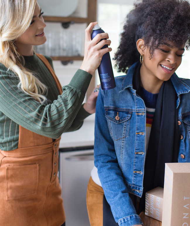 Picture of a female MONAT Market Partner spraying hair spray on a female's hair.