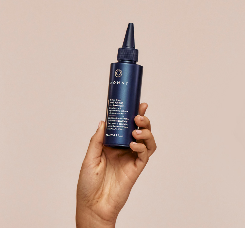 MONAT's Damage Repair Bond-Building Hair Treatment being upheld by a woman's left hand, showcasing the product's aesthetics. Product has a light brown background.