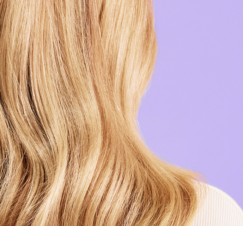 Back head shot of a blonde woman showing her results after treatment. Subject poses in front of a lavender
color background.