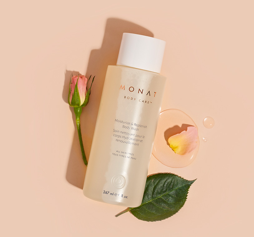 MONAT’s Moisturize & Replenish Body Wash lays centered over a solid peach color background exhibiting its main ingredients such as rose 
         petals & oils ornamenting the main product. 