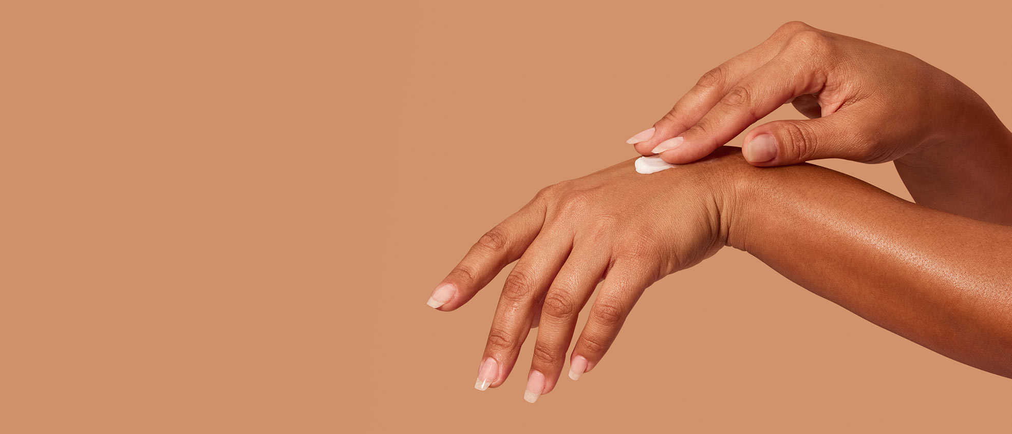 Closeup of a woman’s hands applying MONAT’s Silky & Soothing Hand Cream over a light peach background.