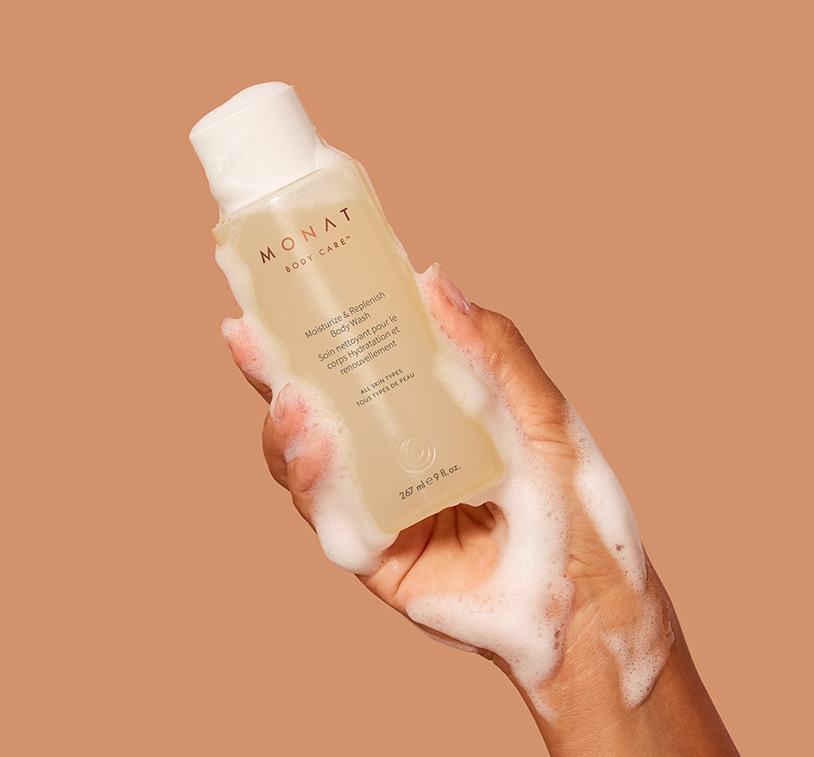 MONAT’s Moisturize & Replenish Body Wash being upheld by a woman’s hand covered in bath foam, 
   showcasing the product’s aesthetics and texture.