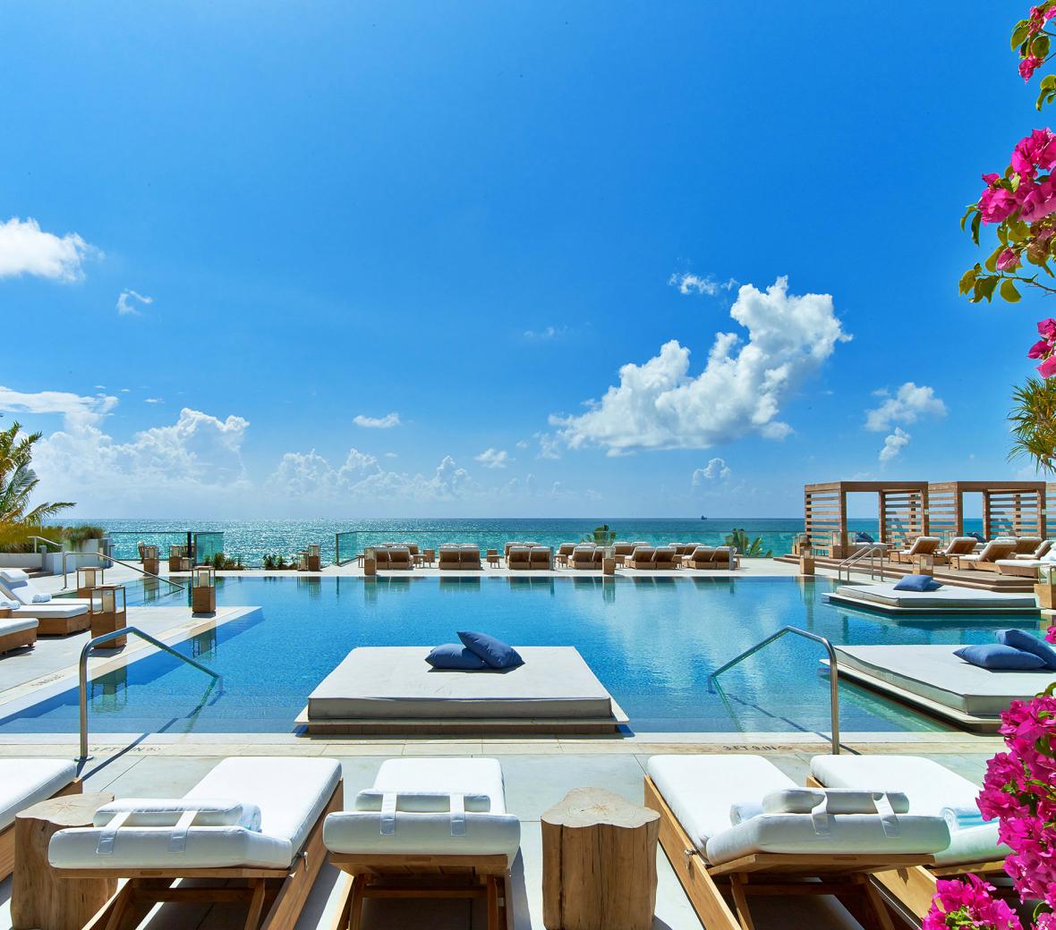 Luxury pool at a hotel by a beach in Miami with lounge chairs and cabanas.