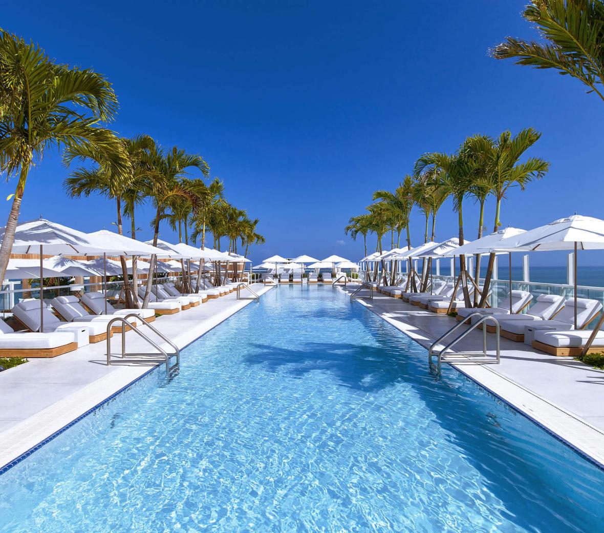 A large hotel pool next to a beach in Miami, with pool lounge chairs around it.