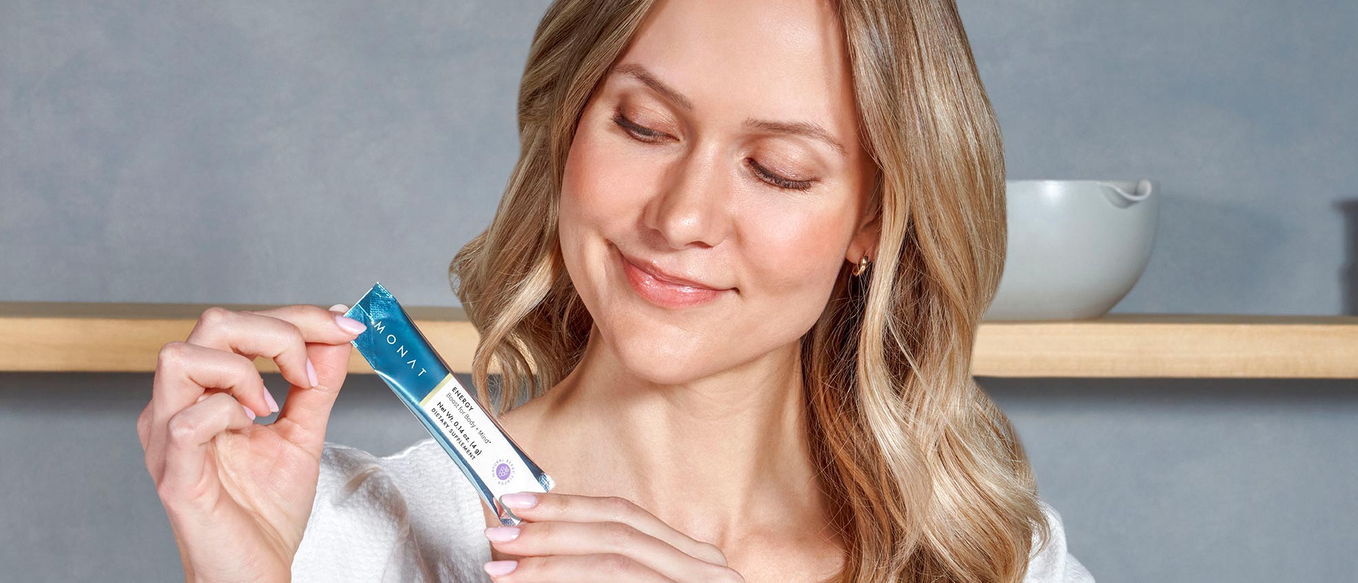 Blonde female holding MONAT Energy™ Natural Berry stick pack.