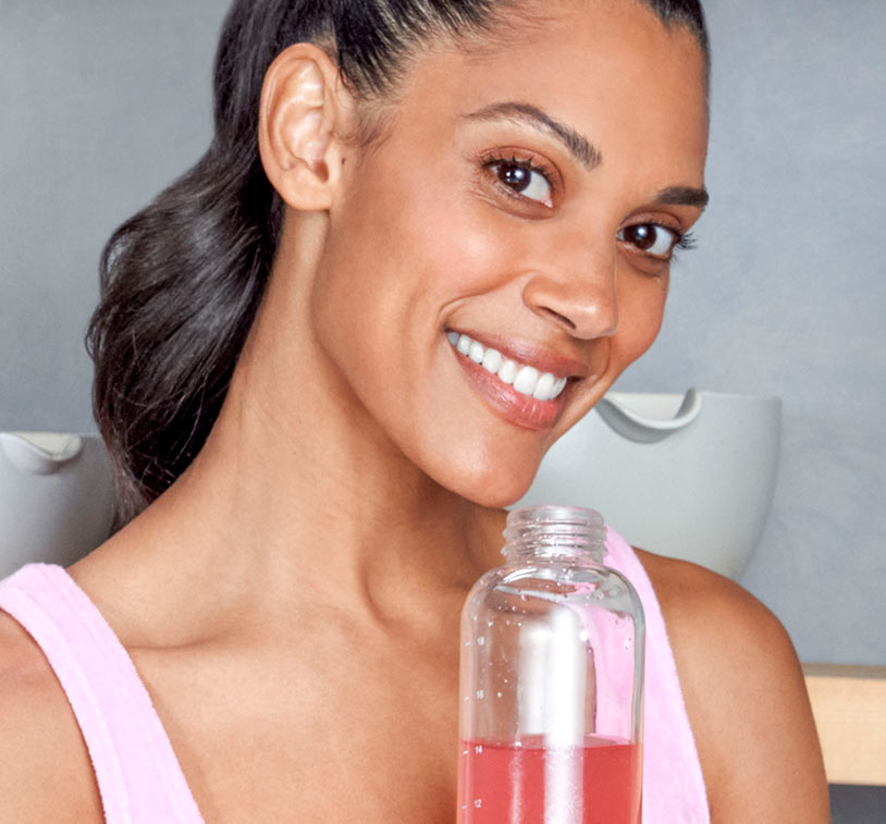 Brunette female while holding a bottle of water mixed with MONAT Energy™ Natural Dragon Fruit.