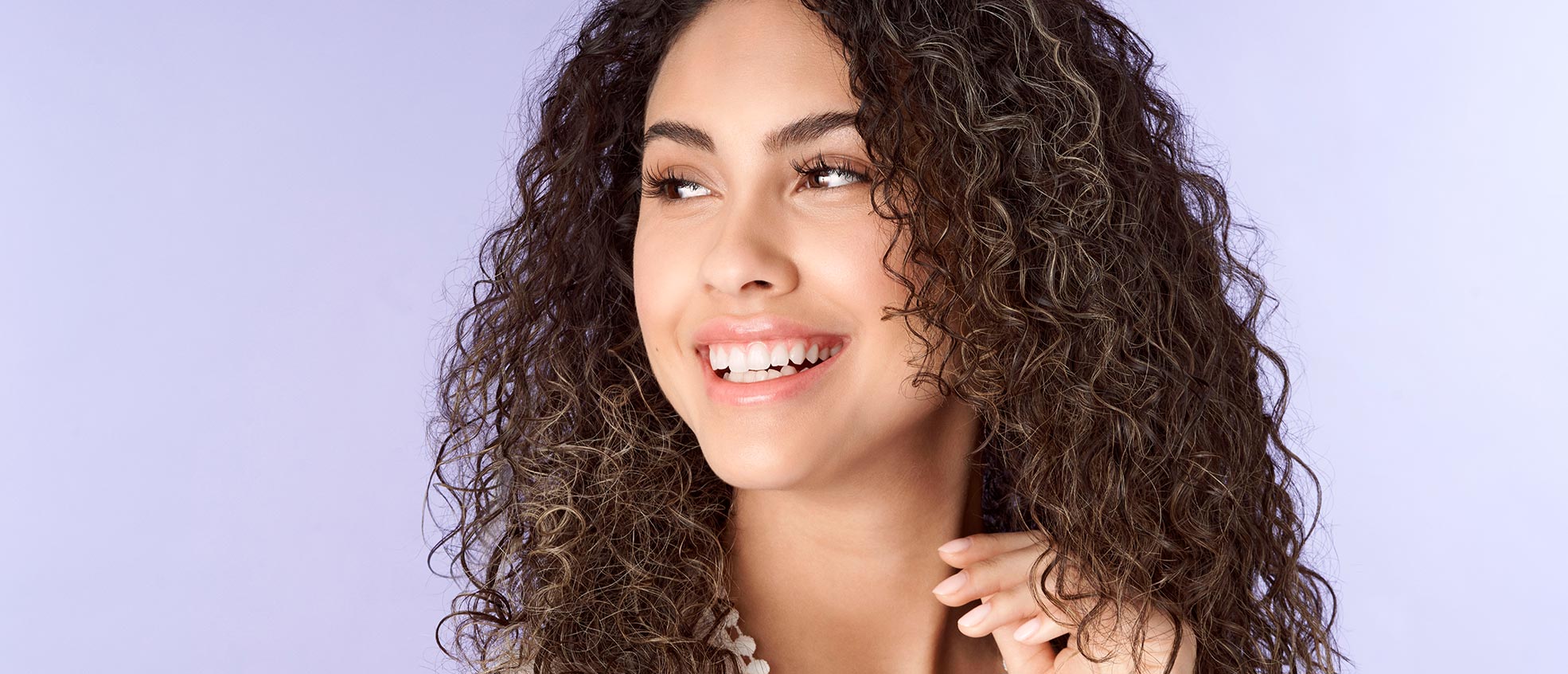 A brunette woman with curly hair smiling and looking to the side.