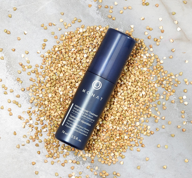 MONAT’s Damage Repair Shampoo stands over a white solid background setting displaying raw ingredients such as oils, citrus & 
				herbs along with additional glass ornaments around it.